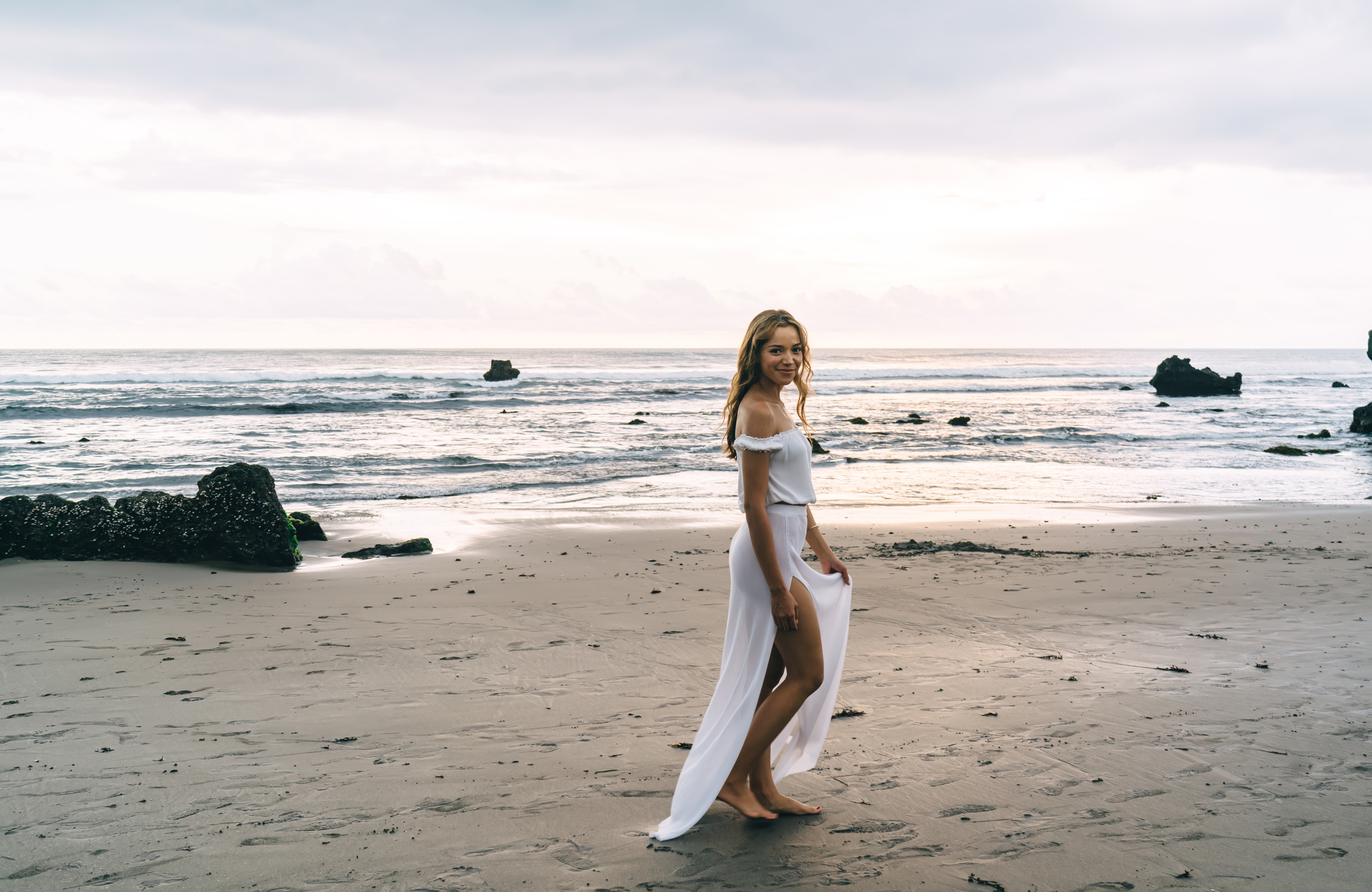 Young Ethnic Woman Walking on Sandy Seashore during Sunset